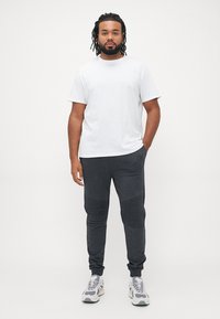 White cotton t-shirt paired with dark grey joggers featuring ribbed accents and sporty shoes, suitable for casual wear.