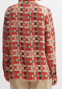 Blusa a maniche lunghe in un tessuto leggero e a trama, caratterizzata da un motivo geometrico in tonalità di rosso, rosa, beige e marrone.