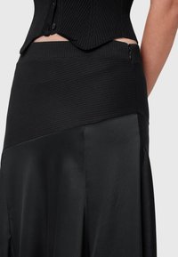 Top corto a coste nero con scollo aderente e gonna nera in satin alta in vita, caratterizzata da una texture liscia e una cerniera laterale.