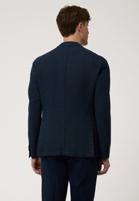 Navy blue blazer with a smooth texture, tailored fit, single vent in the back, and buttoned cuffs. Constructed from lightweight fabric.