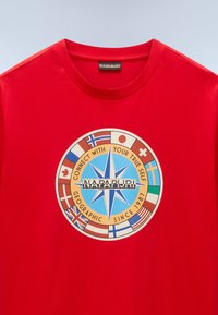 Rød bomulds T-shirt med et rundt grafisk design af et kompas og forskellige landeflag. Teksten inkluderer "FORBIND DIG MED DIN SANDE SELV."