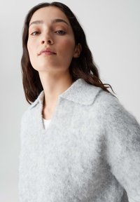 Lichtgrijze, gestructureerde trui met een kraag, met een zachte, fuzzy uitstraling en een licht oversized pasvorm. Model draagt er een wit shirt onder.