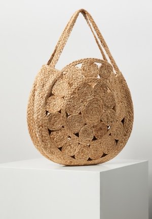 Bolso redondo de paja tejido con asa trenzada y patrón floral circular, exhibido sobre un pedestal blanco contra un fondo liso.