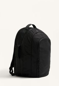 Fekete hátizsák, lekerekített formával, puha, textúrált anyagból készült. Állítható pántokkal és oldalsó cipzáros zsebbel rendelkezik. Minimalista dizájn.