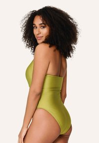Jednodielne plavky v jasne zelenej farbe, charakterizované elegantným dizajnom bez ramienok, hladkou textúrou a vysokým strihom nohavíc.