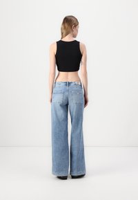 Crni kratki top, svijetloplave široke traperice s džepovima na krpicama, uparen s crnim cipelicama. Glatka tkanina i opušteni kroj.