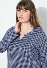 Camiseta de manga larga azul marino con un patrón geométrico blanco. Presenta un escote redondeado con un corte y una tela texturizada para mayor detalle.