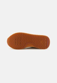 Shoe outsole with a wavy rubber pattern, featuring a brown-orange hue. Smooth texture with rounded edges at the toe.