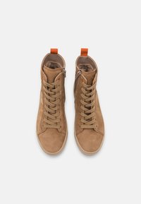 Tan suede high-top sneakers with a textured finish, featuring beige laces, side zipper, and an orange pull tab at the ankle.