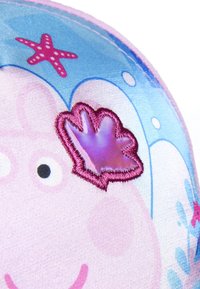 Rosa Stoff mit dem Gesicht eines Comic-Charakters, verziert mit gestickten Akzenten. Der Hintergrund ist blau mit Sternen und Blasen, was Textur und Farbe hinzufügt.