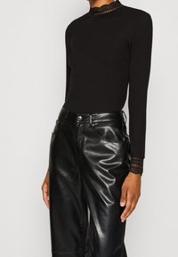 Zwart geribd top met lange mouwen en een geschulpte kanten halslijn, gecombineerd met glanzende zwarte leren wijde broek met voorzakken.