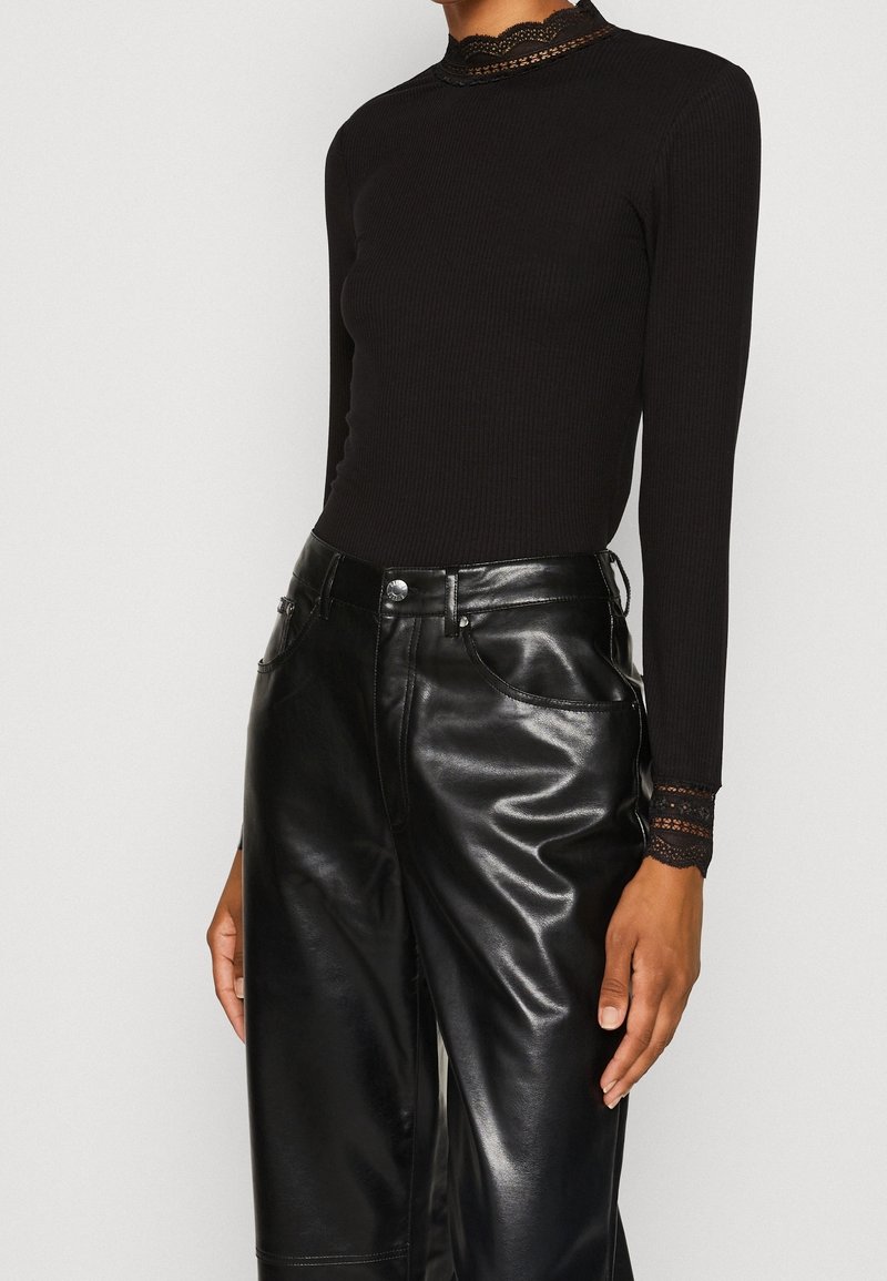 Zwart geribd top met lange mouwen en een geschulpte kanten halslijn, gecombineerd met glanzende zwarte leren wijde broek met voorzakken.