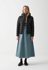 Zwarte pufferjack met capuchon, gestructureerd quiltpatroon, gecombineerd met een lichtblauwe lange rok en zwarte platform schoenen.