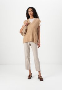 Beige rillet genser vest med V-hals, kombinert med lyse beige skräddersydde bukser. Brune loafers med gull detaljer. Nøytral tote bag.