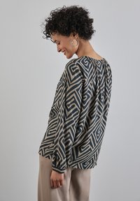 Blusa a maniche lunghe in tessuto stampato con disegni geometrici blu scuri su sfondo beige. Dettagli di scollatura arricciata e polsini.