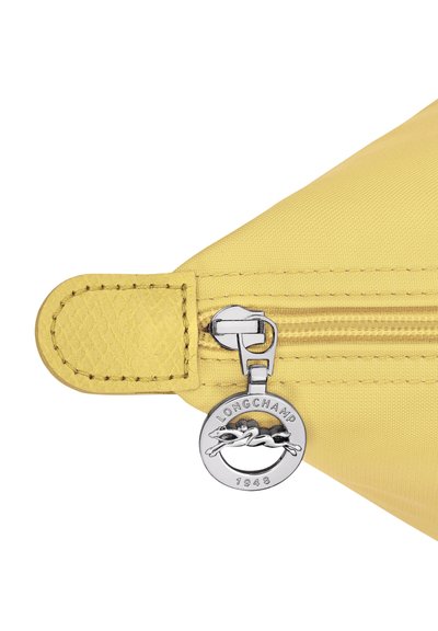 Yellow fabric pouch corner with a metal Longchamp zipper pull featuring a jumping horse logo and the text "LONGCHAMP 1948."