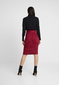 Bourgogne mockaskinn pennkjol med bältesmidja, i kombination med en svart långärmad topp och svarta ankelboots. Slät struktur och figurnära design.