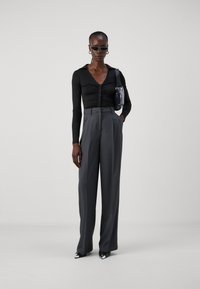 Haut noir à manches longues avec fermeture à boutons, associé à un pantalon gris taille haute ajusté et des escarpins noirs à bout pointu avec des accents argentés.
