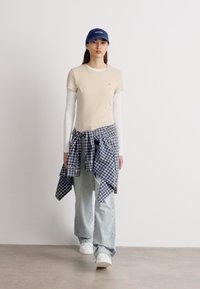 Beige trimmet t-skjorte over en langermet hvit skjorte, lyseblå baggy jeans og en blå caps. En blå og hvit rutet flanellskjorte knyttet rundt livet.