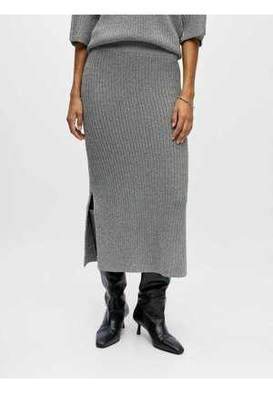 Jupe midi en tricot côtelé gris avec une taille ajustée, fente sur le côté, portée avec des bottines noires à bouts pointus et un haut gris assorti.