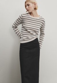 Pull rayé en doux beige clair et marine foncé, associé à une jupe midi noire avec poches et une silhouette ajustée.