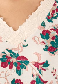 Top a scollo a V con motivo floreale in tonalità verde acqua, bordeaux e rosa. Presenta un delicato bordo in pizzo beige lungo il collo, realizzato in morbido cotone.