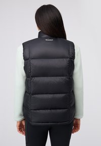 Puffige schwarze Weste mit hohem Kragen und breiten gesteppten Paneelen. Auf der Rückseite befindet sich ein Logo am Nacken. Kombiniert mit einer hellgrünen Fleece-Schicht darunter.