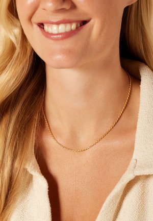 Gouden gedraaide ketting, fijn van textuur met een subtiele glans, rustend op blote huid, complementair aan een lichte, gestructureerde top.