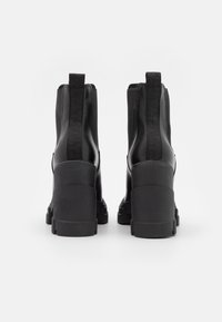 Pár černých masivních platformových bot s elastickými bočními panely a poutky, zobrazených ze zadní strany na bílém pozadí.