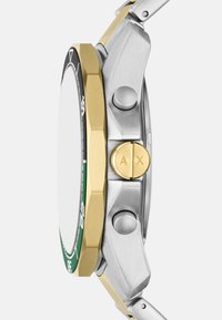 Sidabrinės ir auksinės spalvos metalinis laikrodis su aštuonkampiu rėmeliu, žaliomis ir juodomis detalėmis bei dviem šoniniais mygtukais funkcionalumui.