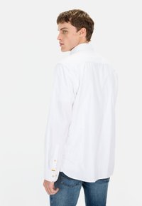 Witte lange mouwen shirt met een button-down kraag, voorzien van gouden knoopdetails op de manchetten, gecombineerd met blauwe spijkerbroeken. Soepele, lichte stof.