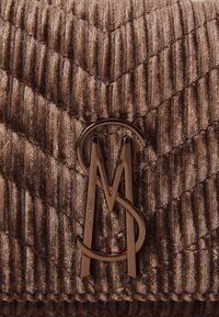 Quilttet brun håndtaske med ribbet tekstur og et markant metallogo i cirkulært design foran.