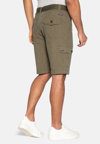 Olijfgroene cargoshorts van duurzame stof. Beschikt over meerdere zakken, een knoopsluiting en een geweven riem. Gemaakt met witte sneakers.