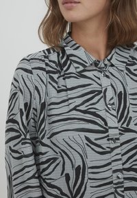 Langärmliges Hemd in Hellgrau mit schwarzen Zebra-Streifen, ausgestattet mit einem kragen und Knopfschluss. Texturiertem Stoff mit dezenten Linien.
