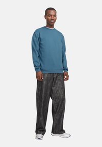 Sweatshirt bleu avec des poignets et un col côtelés, associé à un jean en denim noir ample, présenté avec des chaussures de sport blanches.