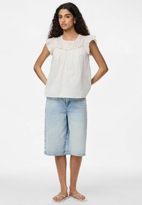 Blusa bianca senza maniche con spalline arricciate e dettagli in pizzo, abbinata a culotte in denim azzurro chiaro e sandali leggeri. Texture liscia.