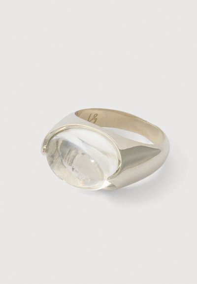 Ezüst gyűrű, amelyen egy nagy, tiszta kő található, sima, fényes szalagon, ívelt formával, modern esztétikát bemutatva.