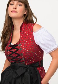 Červený dirndl se květinovým vzorem a černou stužkou, s upnutým živůtkem, krajkovými rukávy a dekorativními kovovými sponami. Černá sukně.