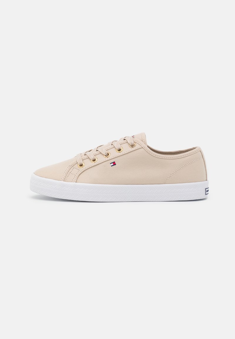 Baskets basses beige avec semelle en caoutchouc blanche, lacets beiges, œillets dorés et un petit logo drapeau rouge, blanc et bleu sur le côté.