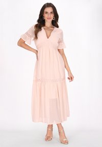 Helle rosa Maxikleid mit Puffärmeln, gepunkteter Textur, tiefem V-Ausschnitt und gestuftem Rock. Getragen mit silbernen Absatzsandalen mit Knöchelriemen.
