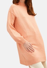 Strickkleid in hellem Pfirsich, mit einem gerippten hohen Kragen, langen Ärmeln und gerippten Bündchen sowie Saum. Weiche Textur mit lockerem Schnitt.