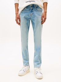 Light blue denim jeans with a slim fit, faded wash, five-pocket design, and a subtle logo on the waistband. Styled with white sneakers.