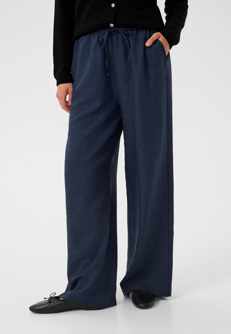 Pantalons larges bleu marine en tissu texturé, avec une taille élastique munie d'un cordon de serrage et des poches latérales.