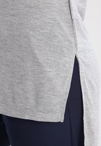 Šedé bavlněné tričko s bočními rozparky, volným střihem a krátkými rukávy. Textura je hladká s melírovaným vzorem.