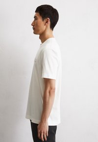 Weißes T-Shirt mit kurzen Ärmeln und rundem Halsausschnitt, aus softem Stoff gefertigt, mit dezenter Logodetaillierung auf der Brust und lockerer Passform.