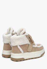 Beige faux-suède enkellaarzen met een witte faux-vachten voering, een gestructureerde rubberen zool en geweven veters. Voorzien van een gewatteerde kraag en dubbele stiksels.