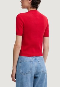 Maglietta rossa a maniche corte in maglia con texture a costine, silhouette aderente e scollo a V, abbinata a jeans di denim azzurro chiaro a vita alta.