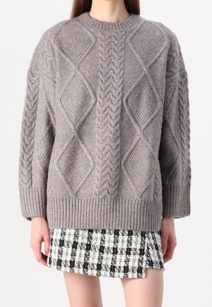 Grau gestrickter Pullover mit Zopf- und Rautenmuster, ausgestattet mit gerippten Bündchen und Saum, über einem schwarz-weißen karierten Rock getragen.