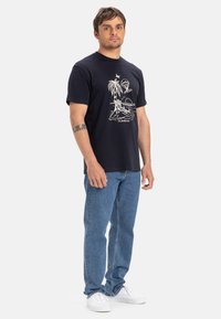 Navy blue cotton t-shirt featuring a white beach-themed graphic, paired with light blue jeans and white sneakers. Simple crew neck design.
