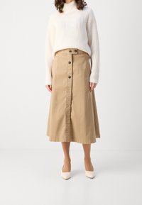 Beige bomullsmidi kjol med knappstängning fram och sidfickor, i kombination med en krämfärgad ribbad tröja och krämfärgade spetsiga klackar.